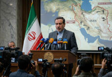 Iranian Foreign Minister Abbas Araqchi addressing the media with the Iranian flag in the background during a briefing on the Iran-US conflict.