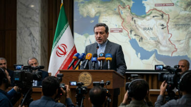 Iranian Foreign Minister Abbas Araqchi addressing the media with the Iranian flag in the background during a briefing on the Iran-US conflict.